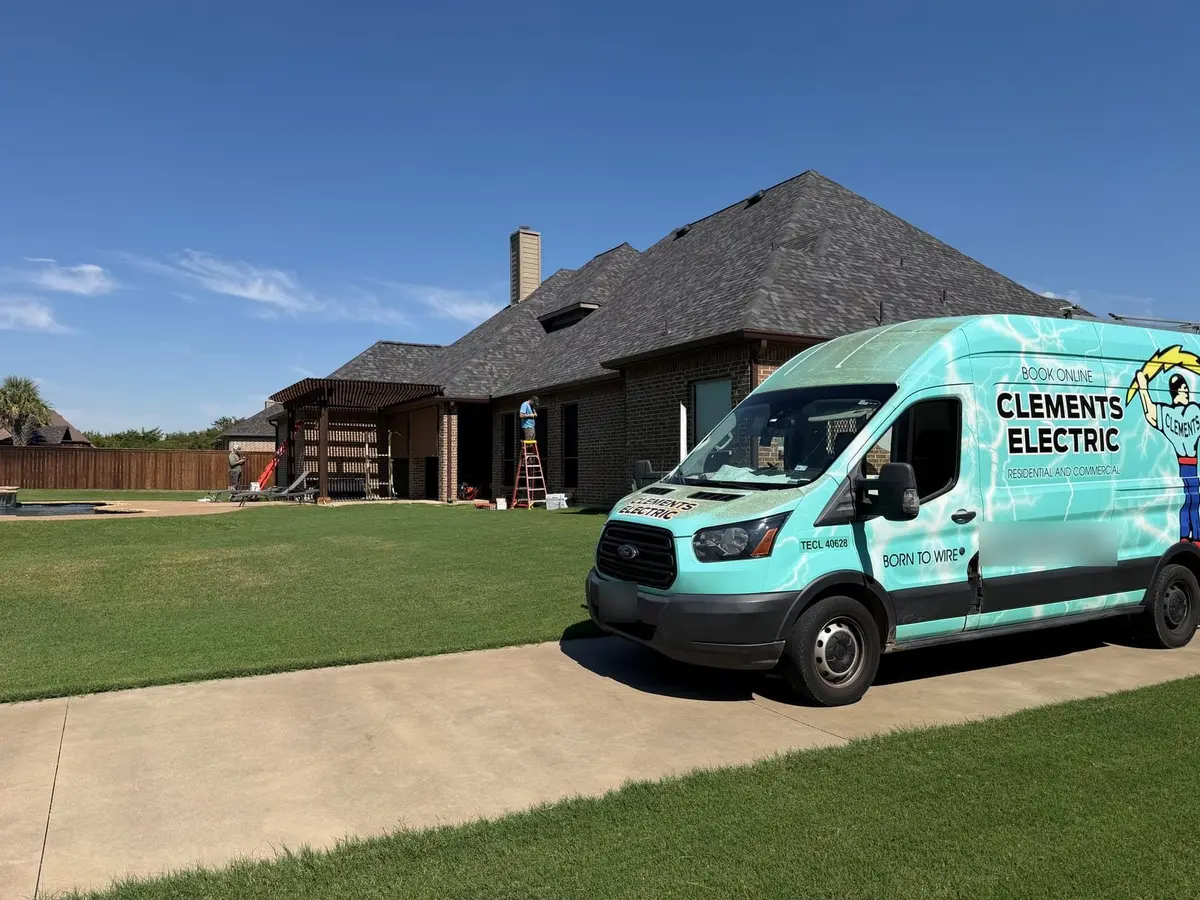 Clements Electric service van parked on the driveway of a brick home in Midlothian, Texas, with ladders set up at the back patio pergola for an outdoor lighting upgrade